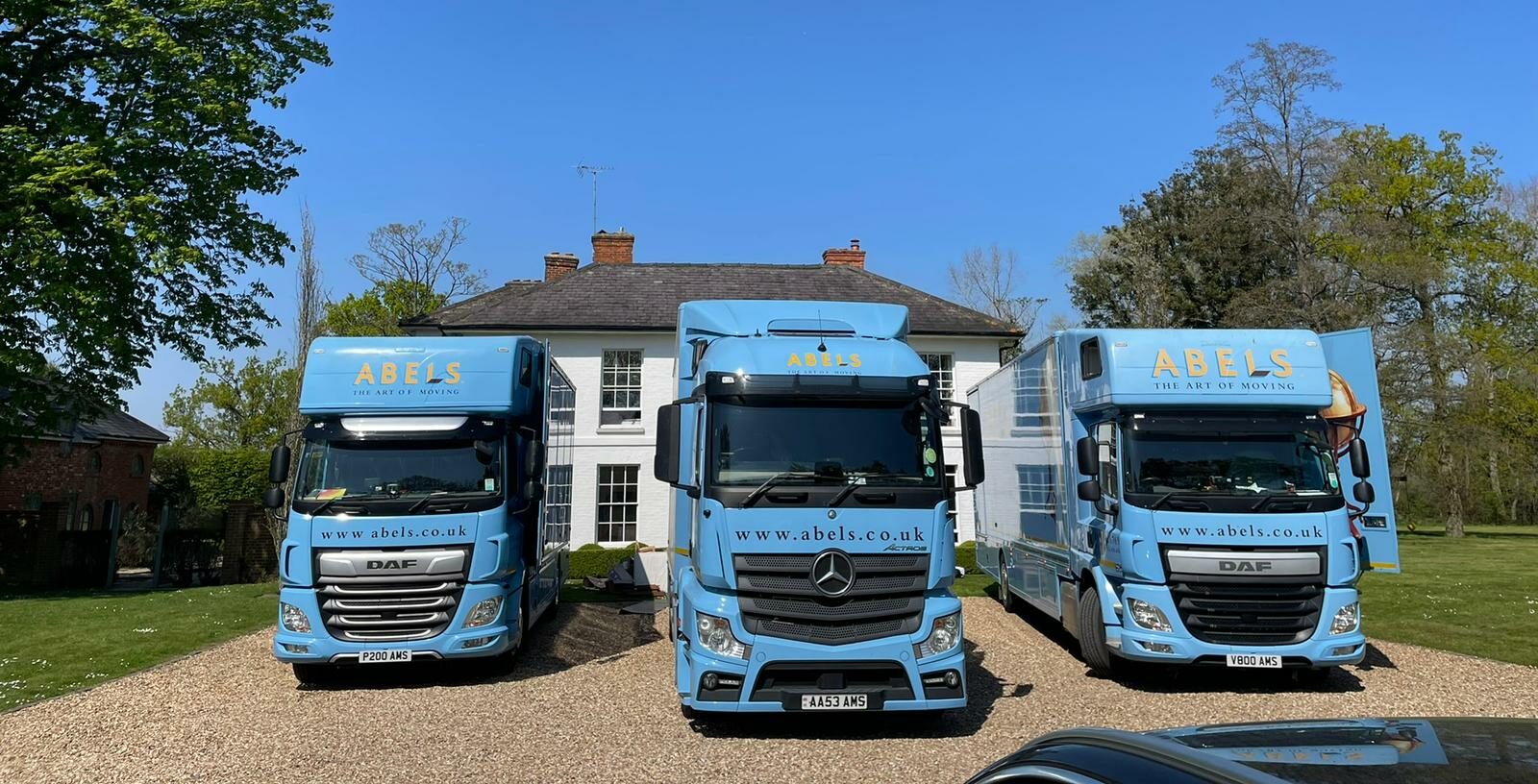 Three trucks from an international relocation specialist company are parked in front of a property, awaiting orders regarding the next steps to take.